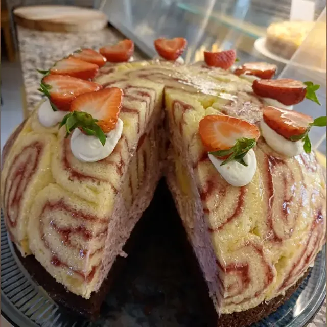 Angeschnittene Erdbeer-Charlotte aus Biskuitroulade mit frischen Erdbeeren in der Theke in Jena