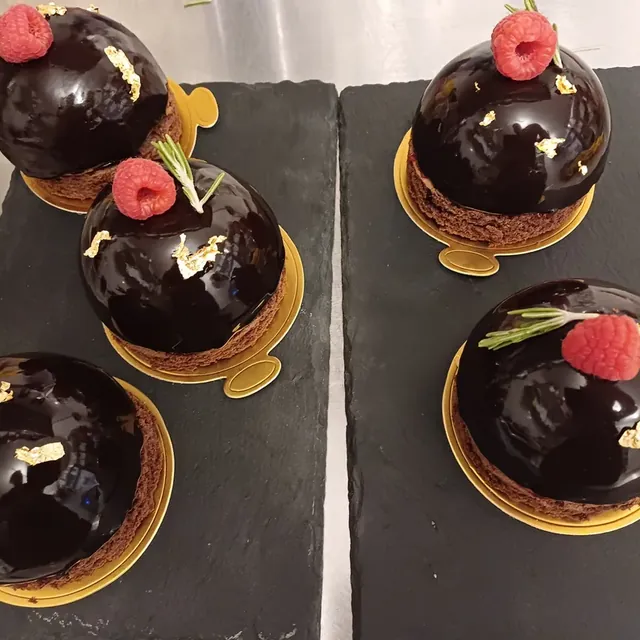 Glänzend glasierte Schokomousse-Kuppeln mit Himbeere, Rosmarin und Blattgold aus der Patisserie in Jena